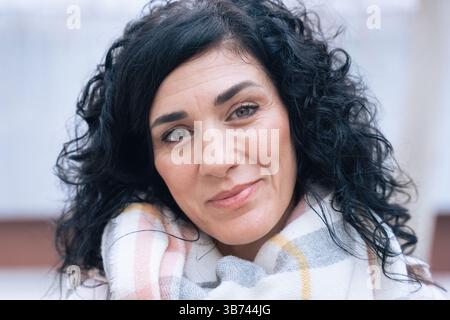 Individuelles Porträt kaukasische Frau mit lockigen schwarzen Haaren und lächelndem Schal Stockfoto