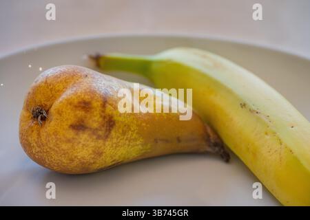 Detailansicht einer Birne und einer Banane in einer weißen Schale auf einem Holztisch Stockfoto