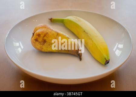 Eine Birne und eine Banane in einer weißen Schale auf einem Holztisch Stockfoto
