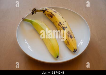 Eine frische Banane und eine reife Banane in einer weißen Schale auf einem Holztisch Stockfoto