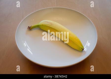 Eine frische Banane in einer weißen Schale auf einem Holztisch Stockfoto
