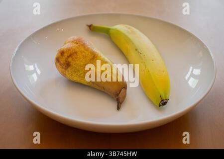 Eine Birne und eine Banane in einer weißen Schale auf einem Holztisch Stockfoto