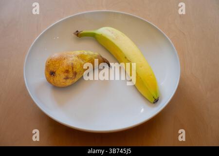 Eine Birne und eine Banane in einer weißen Schale auf einem Holztisch Stockfoto