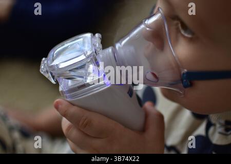 Der kranke Kleinkind benutzt einen kleinen Vernebler, der Luft einatmet. Kind, das Dampf aus einem Inhalator für medizinische Geräte einatmet, Nahaufnahme. Stockfoto