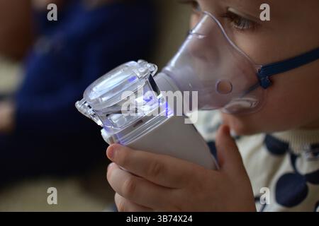 Der kranke Kleinkind benutzt einen kleinen Vernebler, der Luft einatmet. Das Kind atmet Dampf aus einem Inhalator für Medizinprodukte. Stockfoto