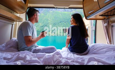 Ein Paar entspannt sich in ihrem Wohnmobil, schlürft einen Kaffee und bewundert den atemberaubenden Fjord, der von üppigem Grün umgeben ist. Perfekt für alle, die Abenteuer und Romantik in der Natur von Lovatnet Norwegen suchen Stockfoto
