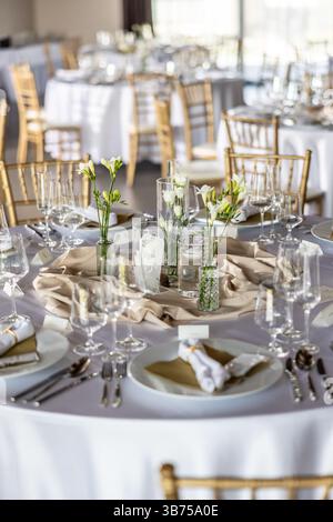 Ein Hochzeitstisch mit einer weißen Tischdecke, dekoriert mit Blumen, Kerzen, Gläsern und Besteck. Stockfoto