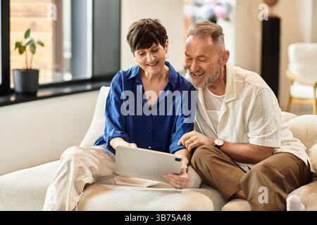 Ein glückliches Paar genießt die gemeinsame Zeit und schaut sich ein Tablet auf der gemütlichen Couch an. Stockfoto