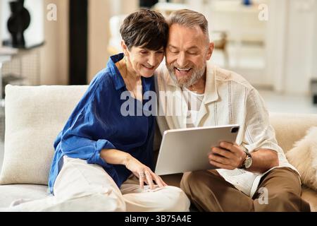 Ein fröhlich verheiratetes Paar genießt eine gute Zeit zu Hause, verlobt mit einem Tablet und teilt ein Lächeln. Stockfoto