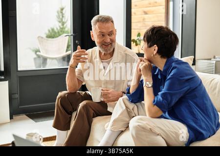 Ein fröhliches Paar mittleren Alters genießt Gespräche und Tee in ihrem einladenden Wohnbereich. Stockfoto