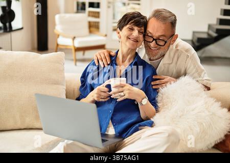 Ein Paar teilt sich einen zärtlichen Moment auf dem Sofa und genießt die Gesellschaft des anderen und ein warmes Getränk. Stockfoto