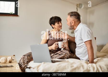 Ein fröhliches Paar genießt ein warmes Gespräch, während es in seinem gemütlichen Schlafzimmer Drinks schlürft. Stockfoto