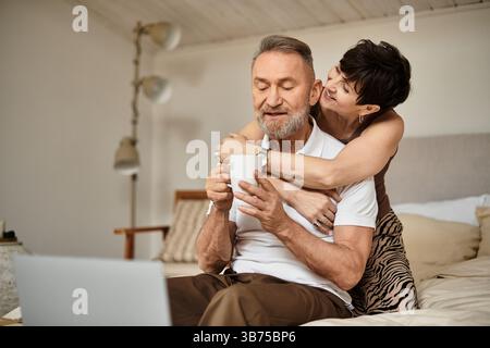 Der Mann mittleren Alters teilt einen freudigen Moment mit seiner Frau, während sie sich zu Hause bei warmen Getränken entspannen. Stockfoto