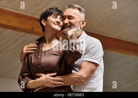 Ein fröhliches Paar mittleren Alters umarmt sich in ihrem warmen, einladenden Zuhause und schätzt ihre Liebe. Stockfoto