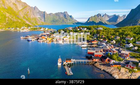Eingebettet zwischen majestätischen Bergen und einem ruhigen Meer bietet dieses farbenfrohe Küstendorf in Lofoten Norwegen klassische skandinavische Architektur. Boote schweben sanft im Hafen unter blauem Himmel. Stockfoto