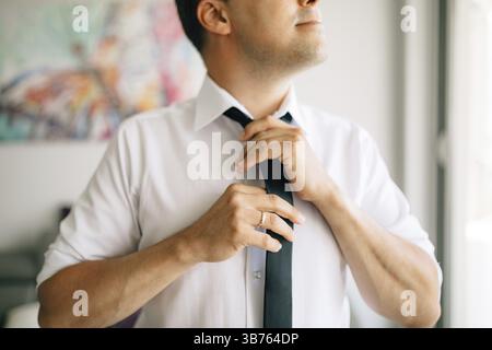 Ein Mann zieht eine Krawatte an, während er sich auf eine Hochzeitszeremonie vorbereitet. Stockfoto