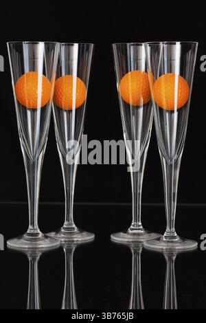 Vier Gläser Champagner mit orange Golfbälle auf der Glasplatte Stockfoto