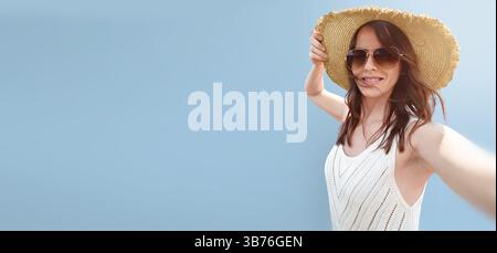 Porträt einer schönen 30-35-jährigen Frau in Hut und Sonnenbrille auf einem leeren Uniform hellblauen Hintergrund, das für Reisen und Touristen geeignet ist Stockfoto