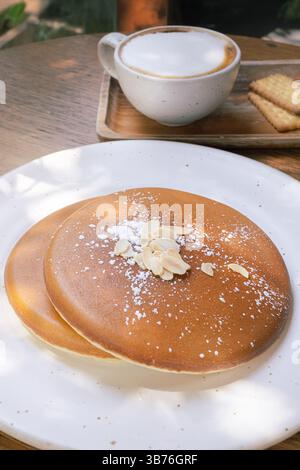 Zwei große Pfannkuchen auf einem Teller in Nahaufnahme. Ein hausgemachtes frisches Frühstück und eine Tasse Kaffee mit Milch unter den Sonnenstrahlen des morgens in einer Nahaufnahme Stockfoto