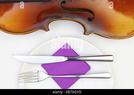 Symphonie des Geschmacks. Weißer Teller und alte Geige auf dem weißen Holztisch. Blick von oben. Flat Lay-Bild Stockfoto