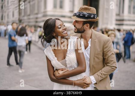 Hochzeit in Florenz, Italien. Der kaukasische Bräutigam umarmt die afroamerikanische Braut an der Piazza del Duomo. Gemischtrassig Hochzeitspaar Stockfoto