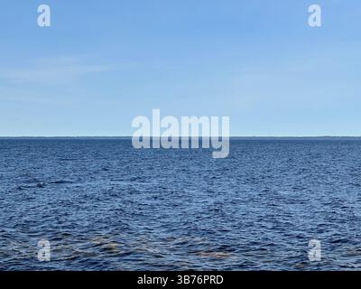 Das riesige blaue Meer erstreckt sich zu einem klaren Himmel und bietet eine ruhige, malerische Aussicht. Stockfoto