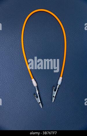 Nahaufnahme eines leuchtenden orangefarbenen Elektrokabels mit Krokodilklemmen an beiden Enden auf strukturierter dunkelblauer Oberfläche, ideal für elektrische und Stockfoto