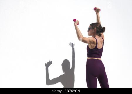 Sportliche Frau, die mit Handgewichten an einer weißen Wand Armübungen im Freien macht Stockfoto