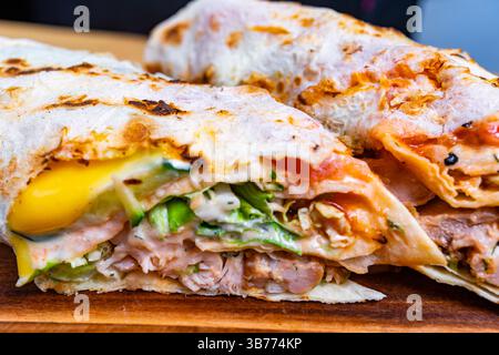 Zwei leckere Wraps sitzen auf einem hölzernen Schneidebrett und präsentieren lebendige Zutaten wie gegrilltes Fleisch, frisches Gemüse und reichhaltige Saucen. Perfekt für einen quic Stockfoto