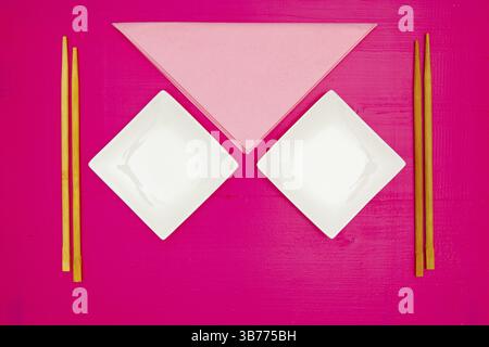 Keramikschalen und Bambus-Essstäbchen für Sushi-Speisen auf dem rosa Holztisch. Draufsicht. Flat Lay-Bild Stockfoto