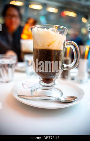 Nahaufnahme eines frisch servierten Wiener Kaffees mit Schlagsahne in einem klaren Glasbecher auf weißem Teller in einem stilvollen europäischen Café. Lifestyle visuell Stockfoto