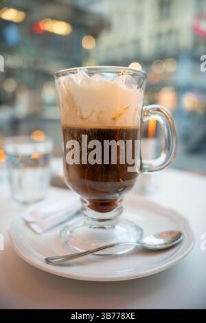 Nahaufnahme eines frisch servierten Wiener Kaffees mit Schlagsahne in einem klaren Glasbecher auf weißem Teller in einem stilvollen europäischen Café. Lifestyle visuell Stockfoto