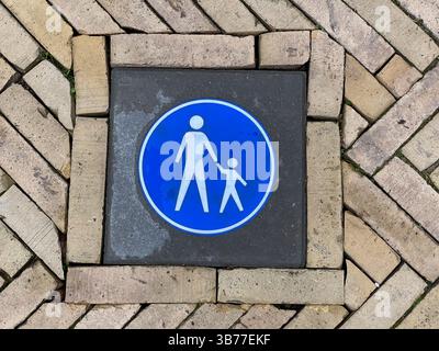 Ein Fußgängerschild, das in einen Gehweg eingebettet ist und ein blaues kreisförmiges Symbol mit weißen Silhouetten aufweist, die eine Gehzone anzeigen Stockfoto