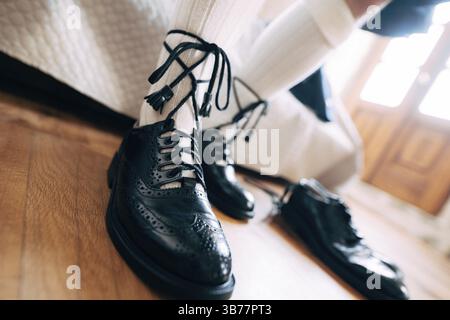 Vorbereitung auf eine schottische Hochzeit. Mann im Kilt, hohe Socken und Schuhe mit langen Schnürsenkeln. In der Nähe ein Paar schwarze Schuhe. Stockfoto