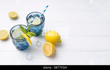 Limonade, Zitronenwasser in blauem Glas, dekoriert mit gelben Zitronen auf leerem weißen hölzernen Leerraum Hintergrund. Sommererfrischung, gesunder Detox Biber Stockfoto