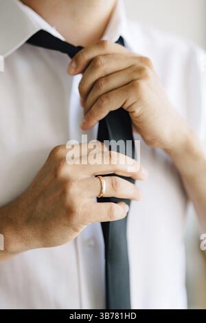 Ein Mann zieht sich an und bindet eine Krawatte, während er sich auf eine Hochzeitszeremonie vorbereitet, Nahaufnahme. Stockfoto