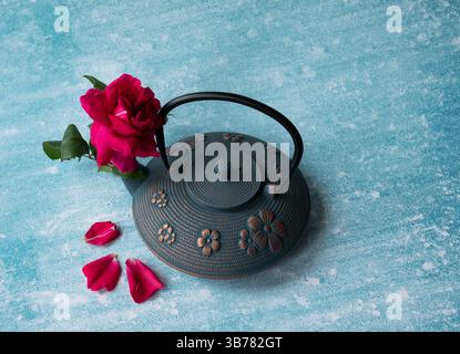 Blick von oben auf die wunderschöne rote Rose in blauer eiserner Teekanne auf blauem Hintergrund. Selektiver Fokus, Kopierraum. Traditionelle asiatische Teezeremonie Stockfoto