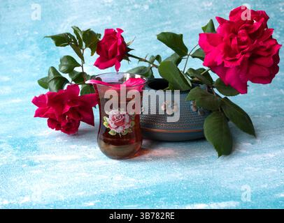 Nahansicht einer schönen roten Rosen in blauer eiserner Teekanne auf blauem Hintergrund. Selektiver Fokus, Kopierraum. Traditionelle asiatische Teezeremonie Stockfoto