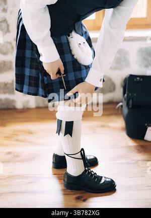 Vorbereitung auf eine schottische Hochzeit. Mann in hohen Socken, Sporran und Schuhen mit langen Schnürsenkeln befestigt ein kleines Schwert am Kilt. Stockfoto