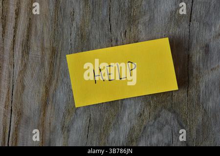 Nachrichtenhilfe auf gelbem Haftnotiz auf texturiertem Hintergrund aus Holzbrett. Der blaue Stift schrieb das Wort "Hilfe" auf das Notizpapier. Stockfoto