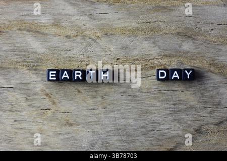 Statement Earth Day aus schwarzen Kunststoffperlen auf gerissenem Holzhintergrund. Begriff des Wortes Erdtag mit Kopierraum. Stockfoto