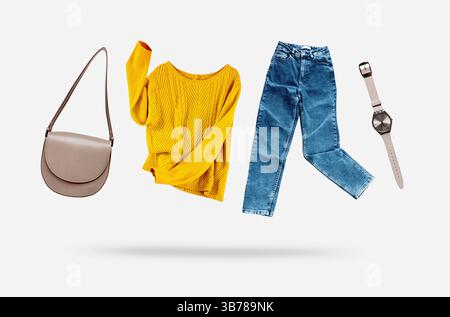 Gelber fliegender Pullover, blaue Jeans, Tasche und Uhren fliegen auf grauem Hintergrund. Trendiges Freizeit Damenbekleidung Set. Damenkleidung Kollektion. Stockfoto