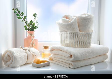 Gefaltete Handtücher stapeln, ätherisches Öl und Seife auf der Fensterbank, leerer Kopierraum. Körperpflegekonzept, Hotelhintergrund, Badartikel. Stockfoto