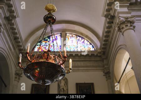 Kronleuchter im Empire-Stil unter der Decke in der Kirche, vor dem Hintergrund eines Mosaikfensters. Ein alter, riesiger Kronleuchter hängt drauf Stockfoto