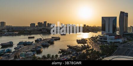 Fesselnder Blick auf den Dubai Creek bei Sonnenuntergang mit traditionellen Booten, modernen Wolkenkratzern und einer leuchtenden Skyline. Das ruhige Wasser reflektiert die Wärme Stockfoto