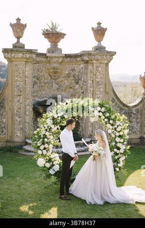 Hochzeit in einer alten Weinkellerei Villa in der Toskana, Italien. Runder Hochzeitsbogen mit weißen Blumen und Grün vor einem alten italienischen Architekten Stockfoto