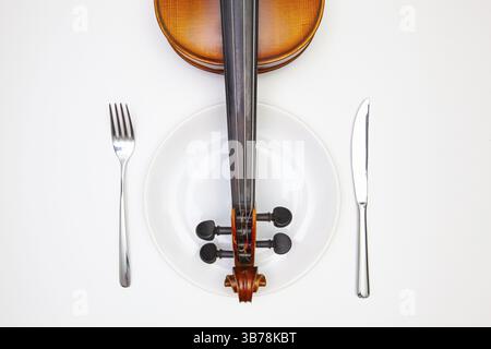Symphonie des Geschmacks. Weißer Teller und alte Geige auf dem weißen Holztisch. Blick von oben. Flat Lay-Bild Stockfoto