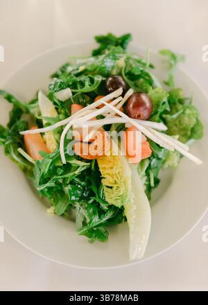 Ein lebhafter Salat mit frischem Gemüse, verschiedenen Gemüsen und Nüssen, der zum Mittagessen in einer weißen Schüssel serviert wird. Stockfoto