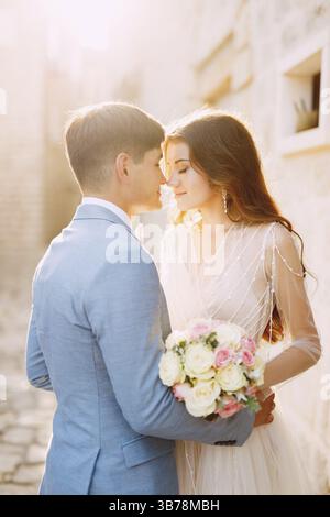 Die Braut und der Bräutigam umarmen sich auf einer wunderschönen alten Straße von Perast in der Nähe einer weißen Steinmauer, Nahaufnahme. Stockfoto