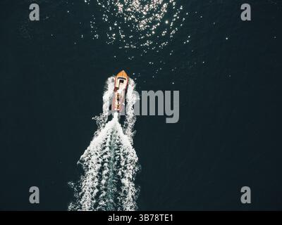 Das Konzept des Luxusurlaubs auf See - ein schönes Holzboot rauscht mit hoher Geschwindigkeit auf die blaue Textur des Meerwassers. Stockfoto